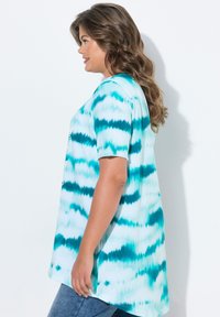 Camisa de manga corta en patrón de teñido anudado en azul claro y teal. Ajuste holgado con dobladillo redondeado, hecha de tela suave. Dos tonos con matices variables.