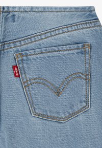 Světlé modré džíny z denimu s výraznou zadní kapsou, která má zakřivený steh a malou červenou etiketu blízko švu.