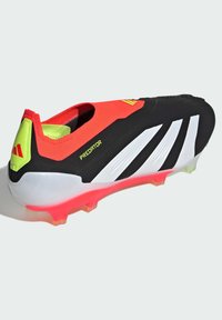 Bottines de football noires, rouges et blanches avec une tige texturée, des rayures blanches en biais et une semelle rose éclatante. Marquage "Predator" visible.