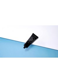 Tube compressible noir avec une étiquette noire comportant un texte blanc, positionné sur une surface bleue contre un fond blanc.