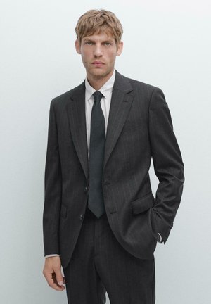 Charcoal grijs gestreept pak met een enkelbreasted jasje, met notch revers en vlakke broek. Gecombineerd met een wit overhemd met kraag en een donkere stropdas.