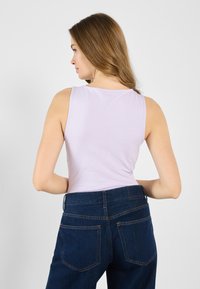 Lyselilla tank topp med rund hals, iført mørkeblå høyhårede jeans med baklommer og kontraststing.
