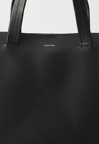 Czarna torba na ramię wykonana z gładkiej skóry, z podwójnymi mocnymi uchwytami i małym białym logo Calvin Klein umieszczonym na środku przodu.