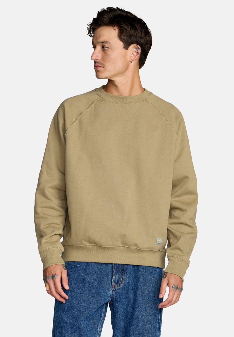 Beżowa bluza z okrągłym dekoltem i rękawami raglanowymi. Wykonana z mieszanki bawełny. Posiada małą naszywkę z logo na dole po lewej stronie.