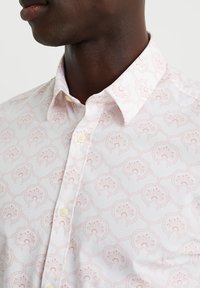 Camisa blanca con un delicado estampado floral en color rosa, con un cuello clásico y cierre de botones, fabricada en tela de algodón liviano.