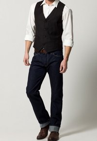 Czarna kamizelka z pięcioma guzikami, noszona na białej koszuli. Ciemne jeansy z denimu z podwiniętymi mankietami i brązowe skórzane buty. Prosty i dopasowany design.