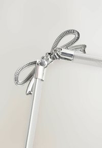 Srebrny metalowy dodatek do włosów z dekoracyjną kokardką, posiadający teksturowaną, żebrowaną rączkę i gładkie wykończenie.