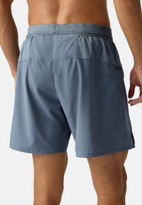 Shorts de sport gris avec une texture lisse, dotés de panneaux latéraux en mesh, d'une taille rétractable et d'une poche arrière pour le rangement.