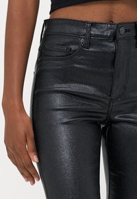 Svarte, høyt midjede jeans med en blank metallisk finish. Har fem lommer, glidelåsfront og en tettsittende silhuett.