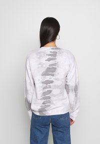 Světle šedá mikina s vázáním barvy tie-dye, volnější střih, dlouhé rukávy a žebrované manžety. Měkká látka s kombinovaným vzorem tmavší šedé barvy.