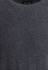 Pull gris foncé réalisé en doux tissu tricoté. Présente un design classique à col rond et une texture minimale avec des éclats subtils. Étiquette de la marque visible.