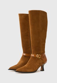 Bottes en suede marron jusqu'aux genoux avec un bout pointu, un talon moyen et une sangle en cuir avec une boucle dorée.