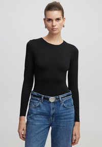 Zwarte longsleeve bodysuit met een aansluitend ontwerp. Gepaard met lichtblauwe high-waisted denim jeans met een zilveren accent als riemgesp.
