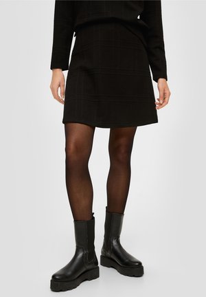 Czarna teksturowana spódnica w kratkę, zestawiona z ciemnymi rajstopami i masywnymi czarnymi botkami z gładkiej skóry.