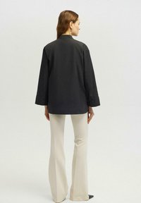 Camisa negra de botonadura frontal con mangas largas, ajuste ligeramente holgado, tejido suave y cuello clásico, combinada con pantalones crema acampanados.
