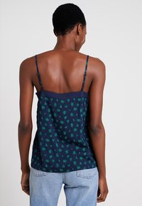 Camisole bleu marine avec des motifs de feuilles vertes, fines sangles réglables et une silhouette ajustée. Tissu doux avec une texture lisse.