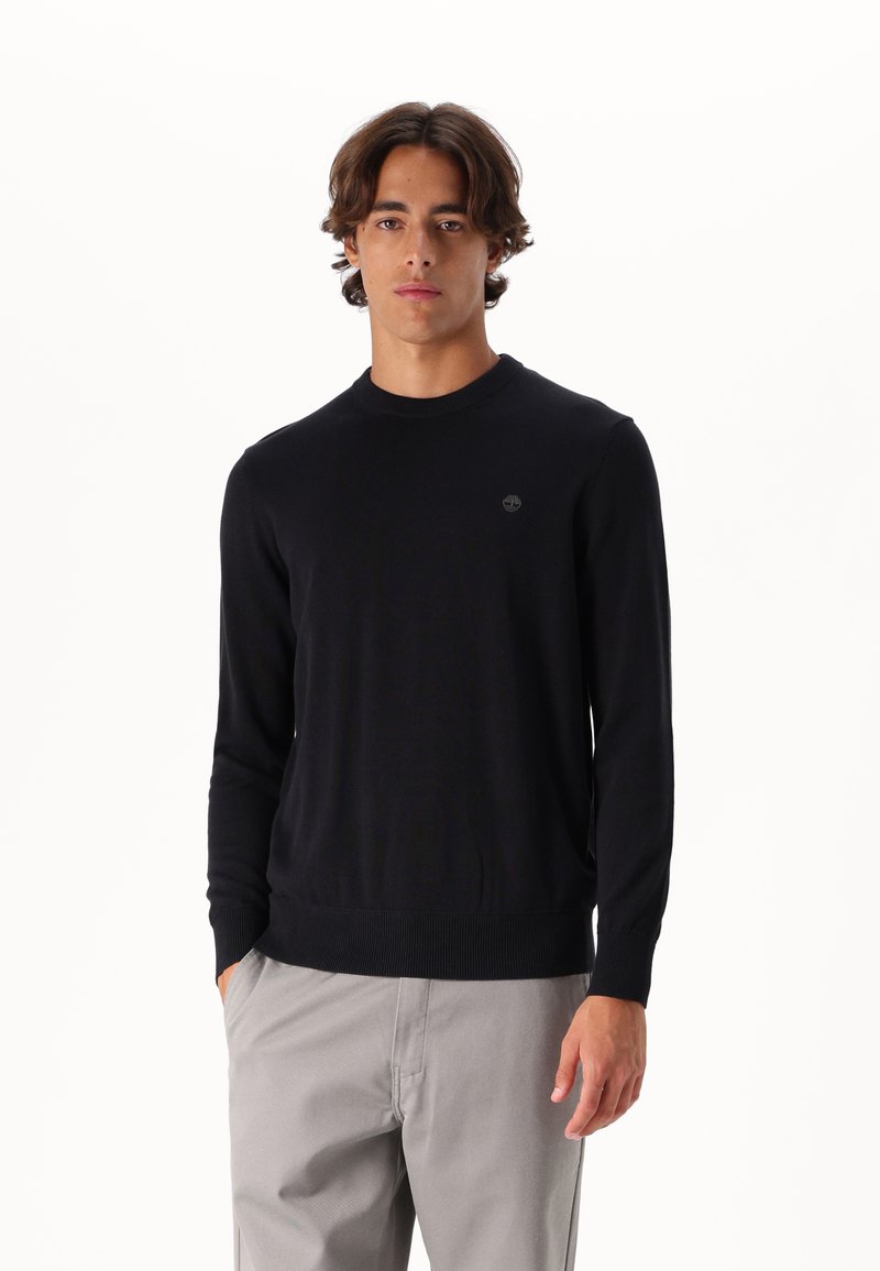 Maglione nero a maglia con collo rotondo, caratterizzato da polsini e orlo ribattuti, arricchito da un piccolo logo sul petto. Texture liscia, design aderente.
