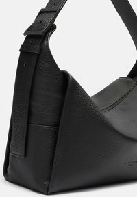Sac à bandoulière en cuir noir avec une finition texturée, forme géométrique et sangle ajustable avec une boucle noire mate.