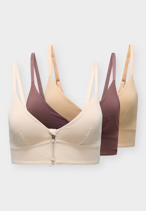 Trois brassières courtes pour femmes, couleur crème, mauve et beige, sont alignées ; la brassière crème à l’avant est dotée d’une fermeture éclair au milieu devant.