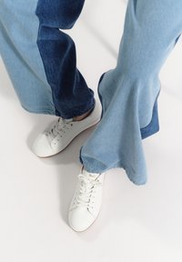 Białe trampki ze skórą o fakturze, złotymi akcentami, zestawione z szerokimi dżinsami z jasnymi i ciemnoniebieskimi panelami.