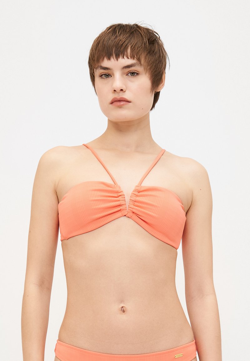 Peach ribbed bikini top with ruched center detail and thin straps. Smooth texture, bandeau shape, suitable for swimwear.