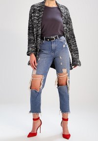 Černobílé pletené bolero, šedé přiléhavé tričko, seprané světle modré džíny s roztrhanými detaily a červené lodičky na vysokém podpatku.