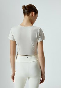 Lys beige cropped t-shirt med korte ærmer og rund halsudskæring, parret med højtsiddende hvide leggings med et lille sort logo.