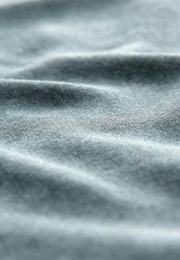 Gråt stof med en blød, glat tekstur; har blide folder og en subtil glans, der fremhæver dets lette og luftige udseende.