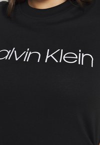 Camiseta negra de algodón con cuello redondo, que presenta el texto del logo en blanco "Calvin Klein" en el pecho, textura suave, mangas cortas.