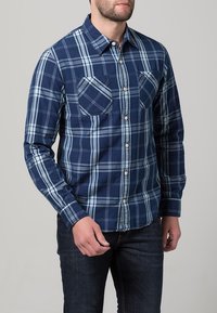 Košile s dlouhým rukávem v námořnické modré a světle modré kostkované s dvěma kapsami na hrudi, vyrobená z měkké tkané látky.