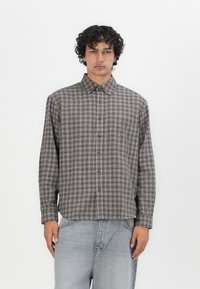 Bruin en beige geruit overhemd met een kraag, lange mouwen en een borstzak, gecombineerd met lichtgrijze denim jeans.