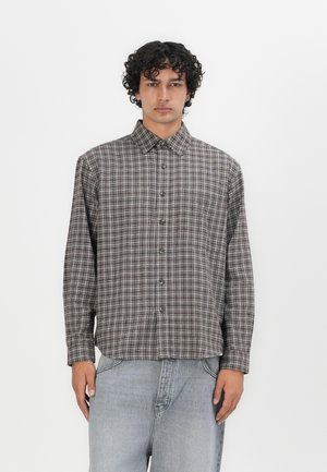 Brown and beige checked button-up shirt with a collar, long sleeves, and a chest pocket, paired with light gray denim jeans.