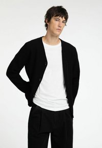 Mustmust koos lõdva lõike, ümmarguse kaelusega, ees nööpidega ja pika varrukaga. Kantud valge T-särgi ja mustade pükstega.