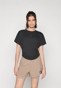 Maglietta sportiva nera a maniche corte con un piccolo logo scuro e pantaloni corti beige con vita elasticizzata e logo sulla gamba. Tessuto liscio.