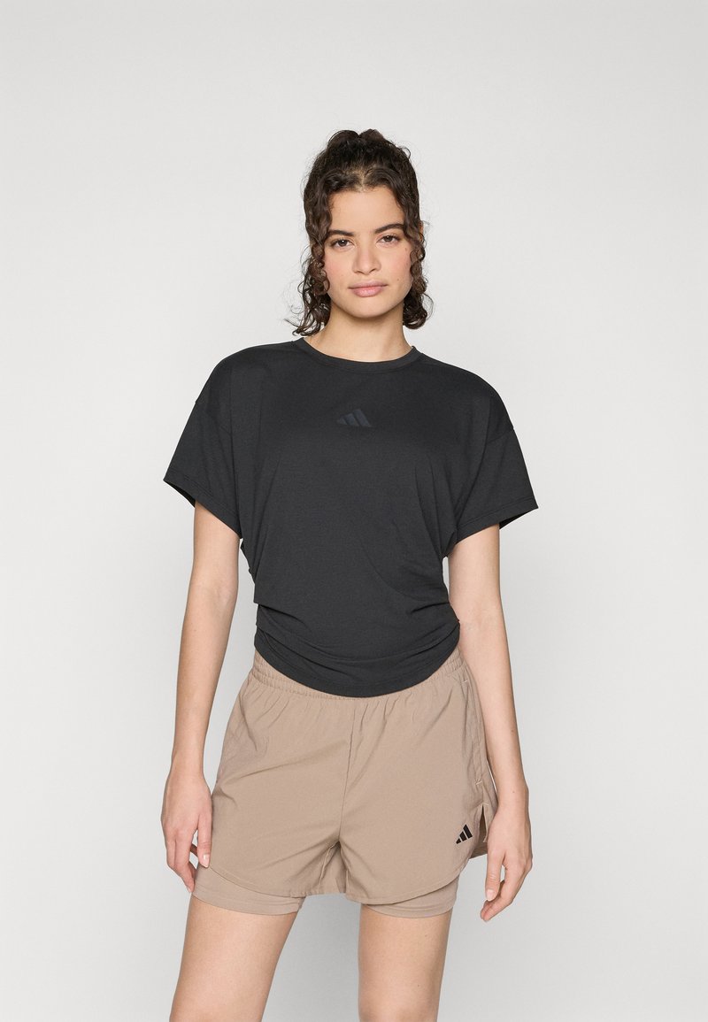 Maglietta sportiva nera a maniche corte con un piccolo logo scuro e pantaloni corti beige con vita elasticizzata e logo sulla gamba. Tessuto liscio.