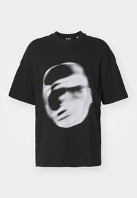 Black oversized t-shirt made of cotton featuring a blurred white face graphic in the center. Ribbed crew neckline, short sleeves.