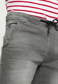 Pantalones de mezclilla gris con cintura ajustable, que cuentan con bolsillos laterales y una textura suave. El diseño incluye detalles de costura sutiles.