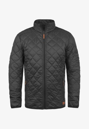 Sort quiltet jakke med høj krave, foran lynlås og tan akcenter. Har skrå syninger og sidelommer. Letvægtsmateriale.