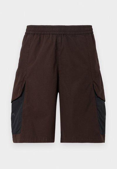 Shorts marron avec une ceinture élastique, dotés de panneaux latéraux noirs et de poches passepoilées. Le matériau semble léger avec une texture lisse.