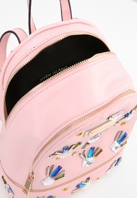 Růžový kožený batoh s dekorativními drahokamy v různých tvarech a barvách. Dvojité zipy nahoře s černou podšívkou.