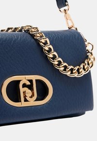 Borsa a tracolla in pelle blu navy con catena dorata, hardware con logo e superficie texturizzata, caratterizzata da una forma strutturata.