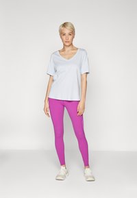 Light blue V-neck t-shirt paired with form-fitting, bright pink leggings, worn with light-colored athletic shoes. Simple, casual design.