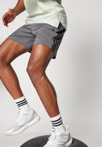 Gray athletic shorts with three black stripes on the side, white sneakers with textured design, and white socks with black stripes.