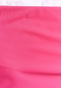 Fuksia puuvillakangas, jolla on sileä rakenne, näkyy selvästi. Yläreunassa on valkoista kangasta, joka kontrastoi alla olevan kirkkaan vaaleanpunaisen kanssa.