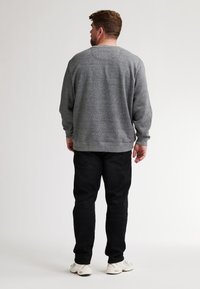 Sudadera gris con cuello redondeado y puños acanalados, combinada con jeans negros y zapatillas blancas; vista desde la parte posterior.