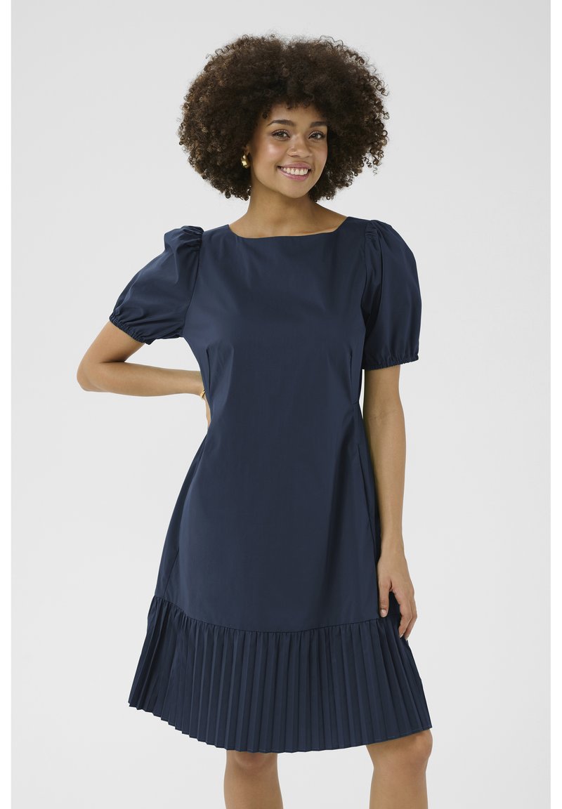 Námornícky modré šaty s krátkymi puff rukávmi, štvorecovým výstrihom a skladanou sukňou. Majú hladkú tkaninu a priliehajúci korzet.