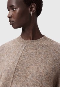 Maglione beige lavorato a maglia con collo rotondo, caratterizzato da un motivo testurizzato e un design a maniche raglan. Il modello indossa semplici orecchini a bottone.