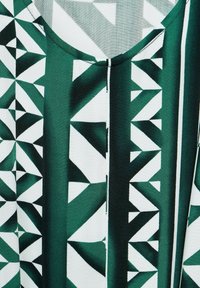 Zelená a bílá tkanina s vzorem, která obsahuje geometrické tvary; hladká textura s kulatým výstřihem a vertikálním pruhovaným designem.