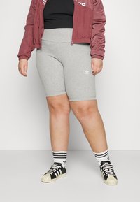 Grå stretchiga cykelbyxor, åtsittande design, med en liten vit logotyp på vänster ben. Tillsammans med en vinröd bomberjacka och svarta sneakers.