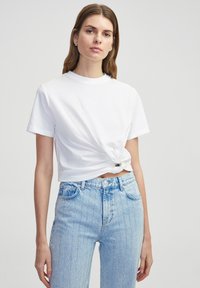 Witte cropped t-shirt met een gedraaide knoopdetail bij de taille, gecombineerd met lichtblauwe denim jeans met verticale strepen en een knopenfly.